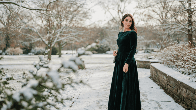 Woman in a long sleeve velvet winter wedding guest dress smiles at an outdoor event.
