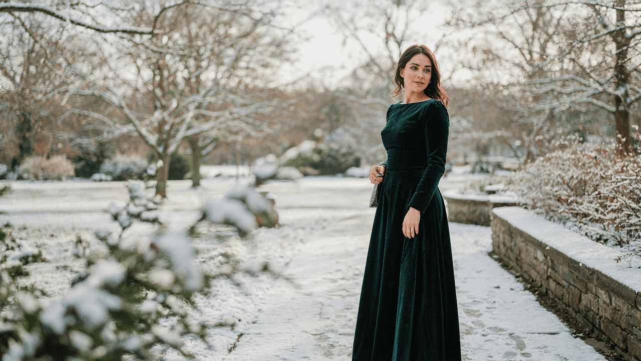 Woman in a long sleeve velvet winter wedding guest dress smiles at an outdoor event.