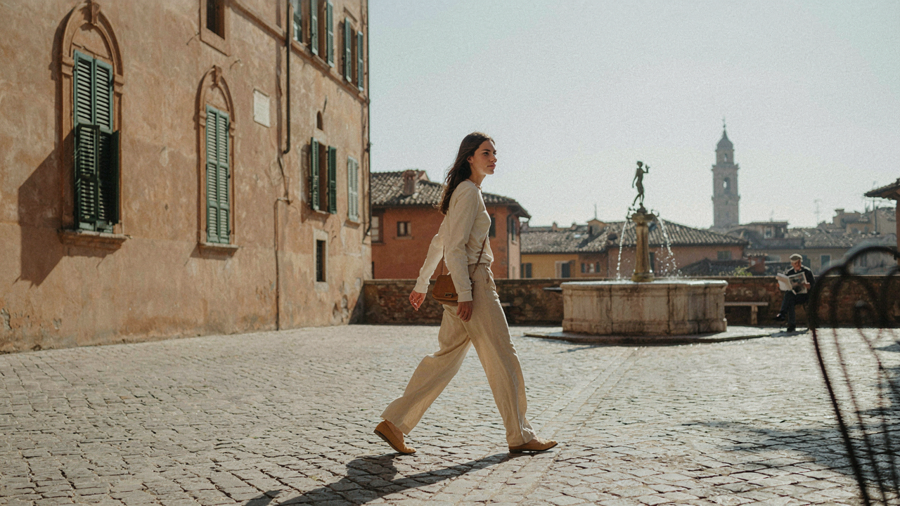 A person in light clothing walks through a sunny Italian piazza, suitable for summer heat.