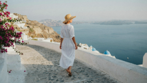 Woman in white linen dress and straw hat walking along a path overlooking the sea.
