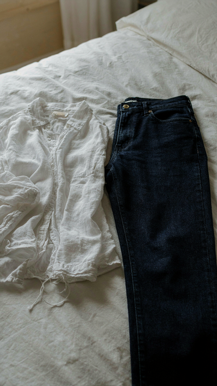 A crumpled linen shirt and stiff dark denim jeans lie next to each other.