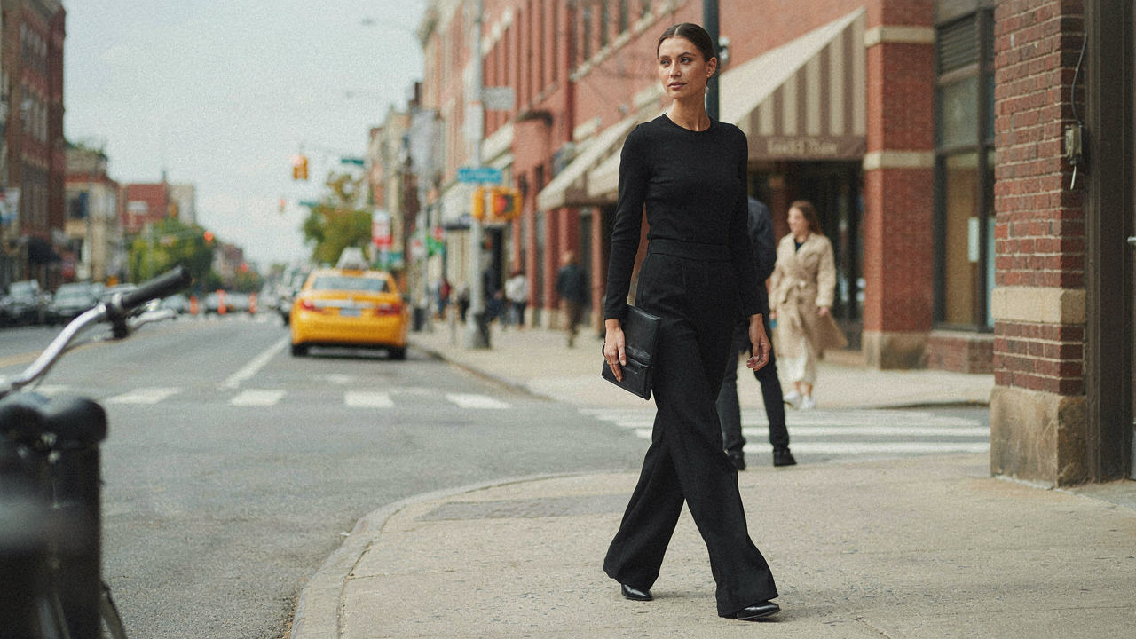 A woman confidently walks in a black wide leg jumpsuit formal on a city street.