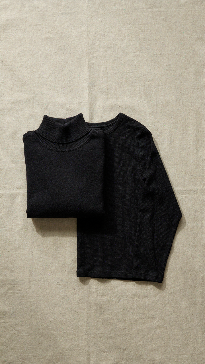 A black merino wool turtleneck and a black thermal shirt are neatly folded.