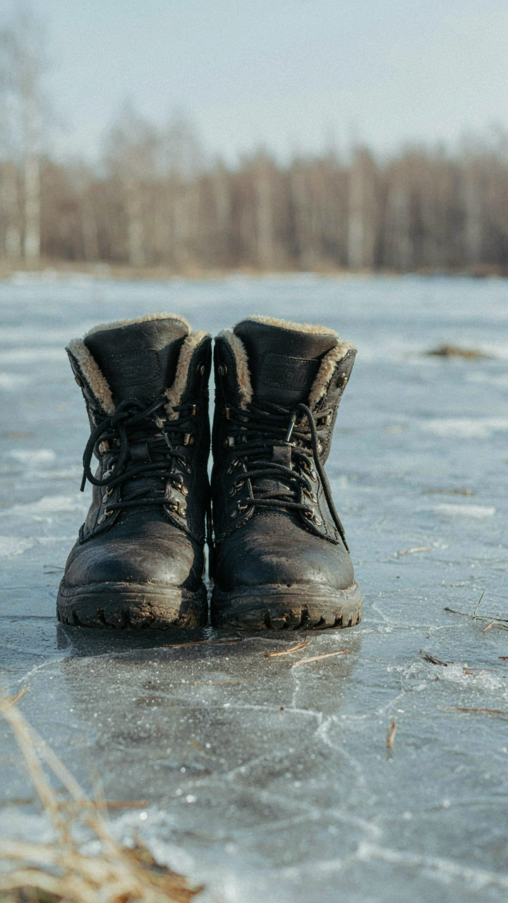 A pair of insulated winter boots with aggressive lugged soles stands on ice.