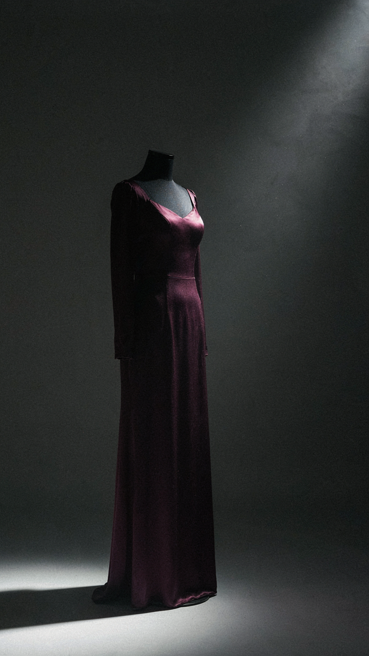 A deep plum silk charmeuse formal dress on a display form with dramatic shadows.
