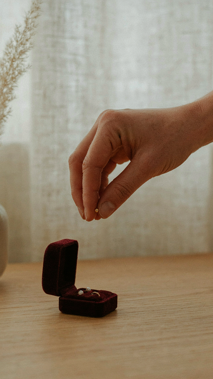 A hand chooses one elegant stud earring from a jewelry box.