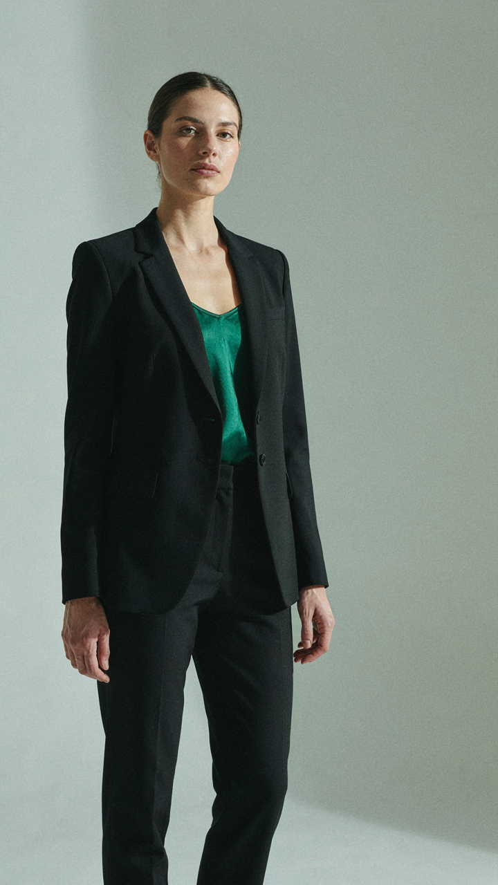 A woman in a structured dark blazer and a jewel-toned camisole stands confidently.