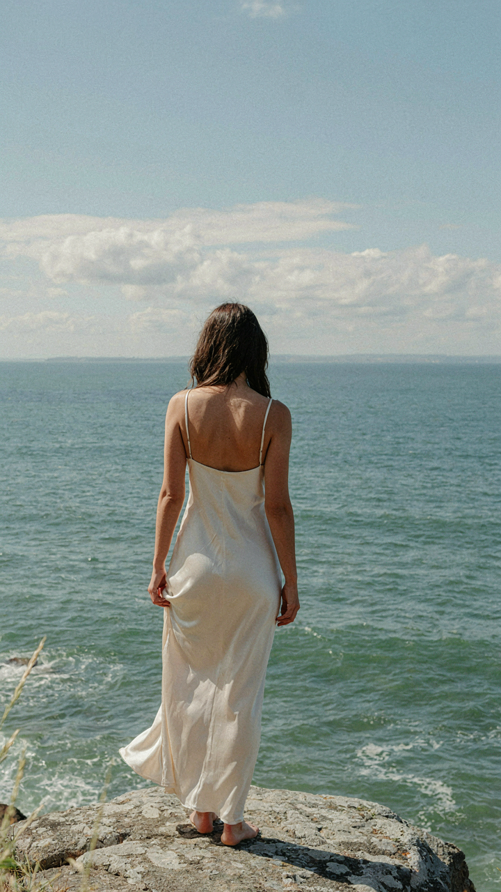 Woman with serene expression looking at the ocean, feeling confident.