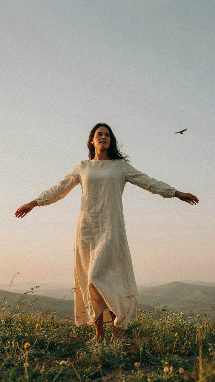 Woman in a long dress stands on a hilltop, embodying an intention.