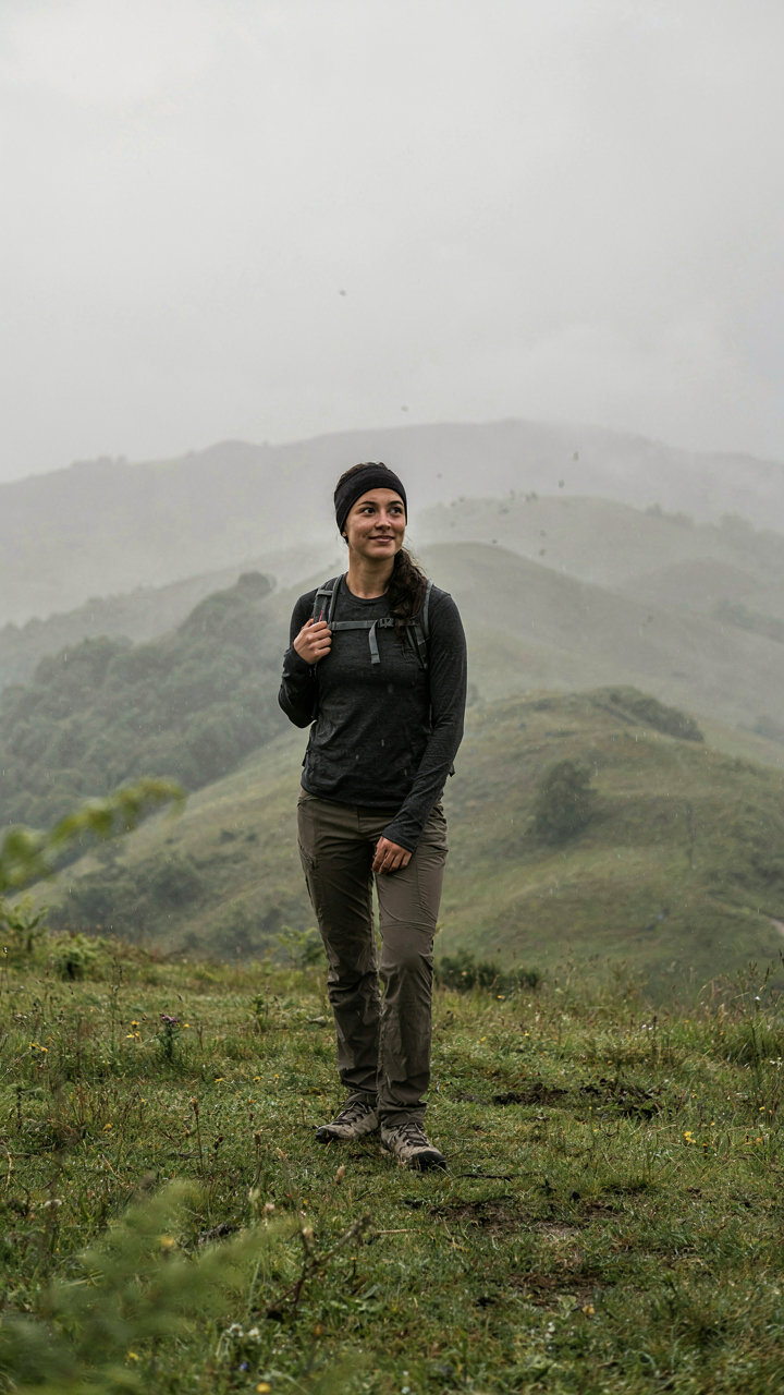 A person stands confidently in quick-dry clothes in a rainy landscape.