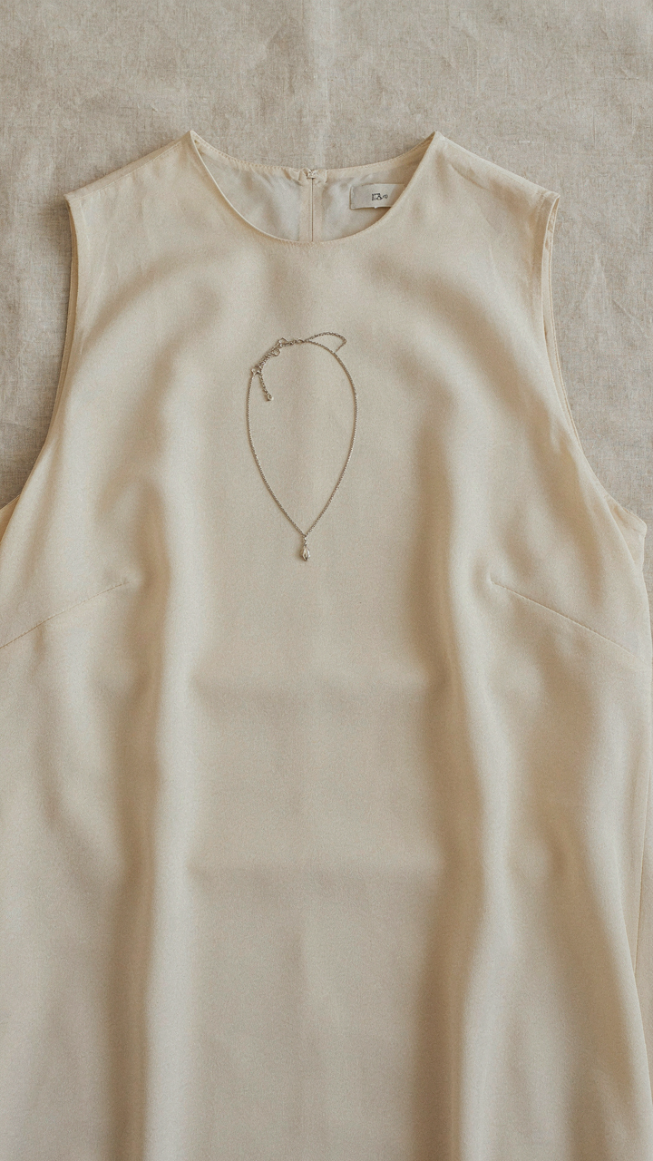 A delicate silver chain lies next to a high crew neck dress.